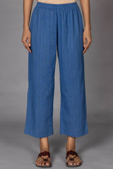 A person standing wearing relaxed fit blue trousers with an elasticated waist, paired with brown sandals.