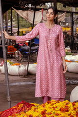 Woman in a pink dress standing among flowers at an outdoor market.