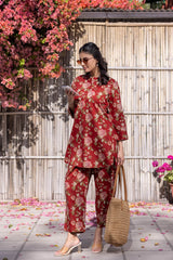 Woman in a red floral outfit standing outdoors with flowers and a wooden fence in the background