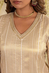 Close-up of a woman wearing a beige and gold striped V-neck kurta with gold embroidery around the neckline, paired with a gold beaded choker necklace.