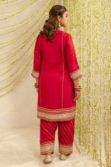 A woman modeling a red three-piece traditional outfit with gold embroidered borders, shown from the back against a draped cream and gold sequin backdrop.